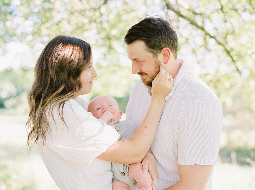 Parents holding their baby while smiling at each other in dappled light under a tree at Old Slate Farm | Family Photographer in Ohio | Anna Laero Photography