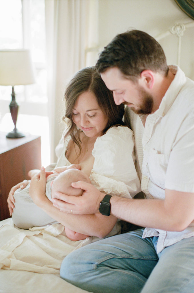 Parents smile down at nursing infant all in white in Modern Farmhouse bedroom at Old Slate Farm nursing | Ohio Family Photographer | Anna Laero