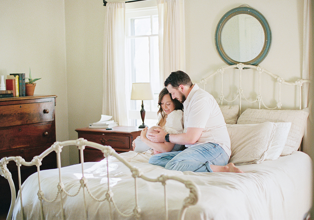 Parents on white bed with metal frame snuggling baby minimalist modern farmhouse style at Old Slate Farm 