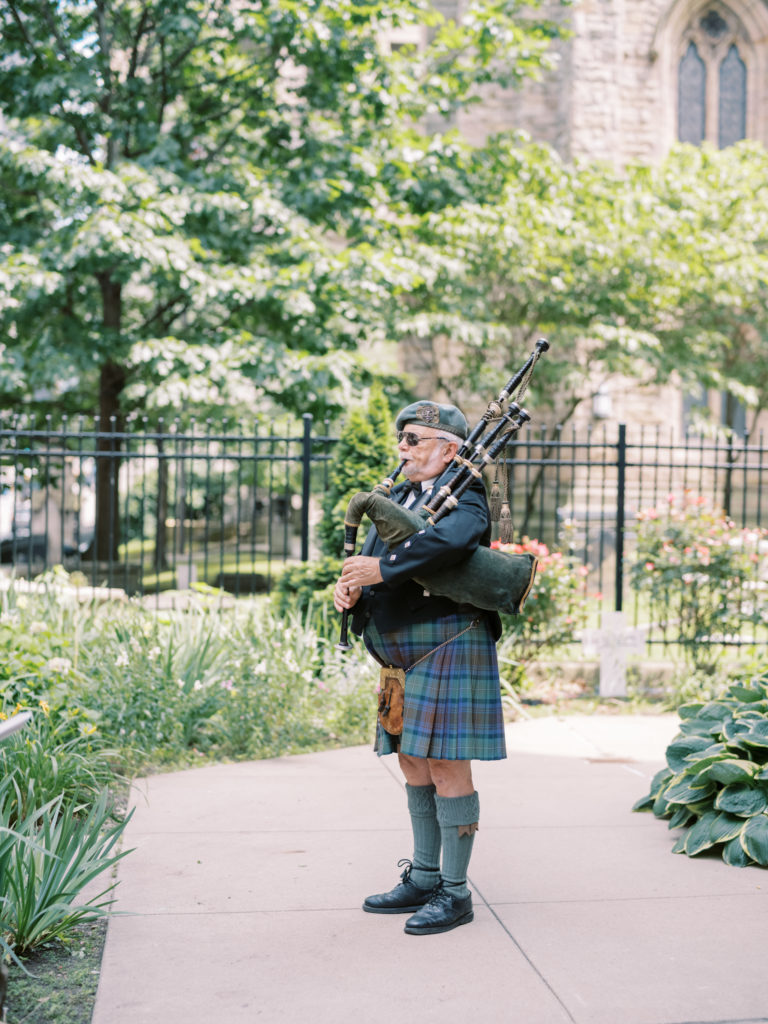 A bagpiper stands outside the church playing music to welcome the guests to this Pittsburgh wedding.