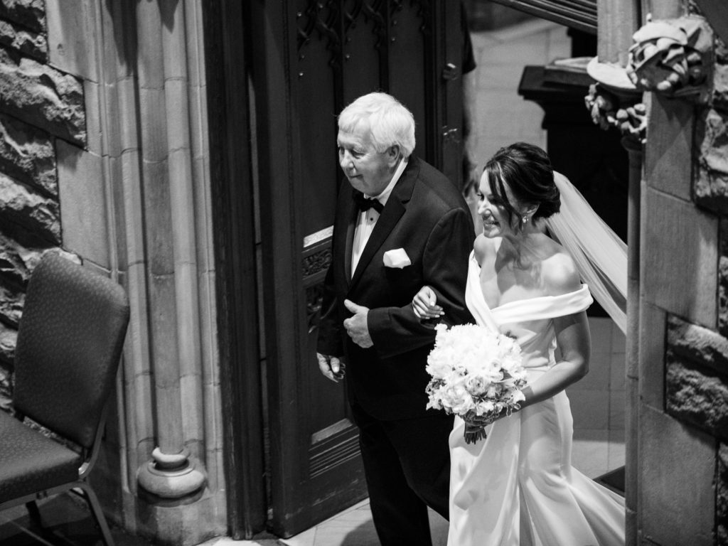 The bride and her father smile with joy as they begin to walk down the aisle in this black and white Pittsburgh wedding photography image.