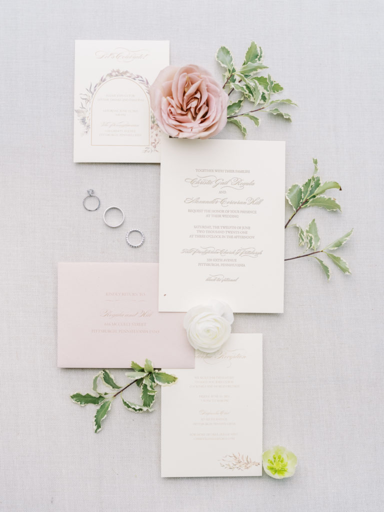A flat lay with flowers, rings and greenery showing off the invitation by K Flower Designs for this wedding in Pittsburgh at Penn Station.